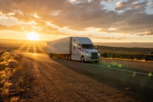Semi-truck hauling a dry van trailer along a rural highway at sunrise, representing long-haul freight transportation and nationwide trucking services.