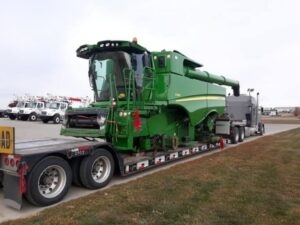 Green John Deere combine harvester secured on a lowboy trailer with wide load signage for oversize transport