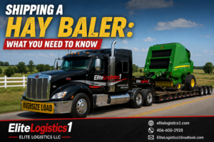 Green round hay baler secured to a flatbed trailer for transport by Elite Logistics LLC on a rural highway.