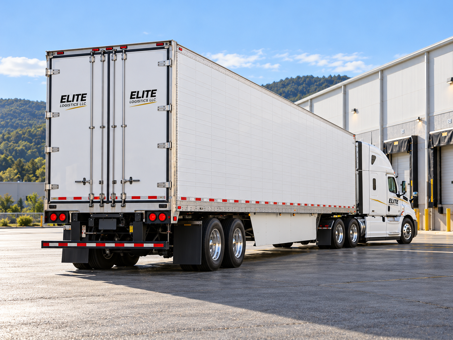Rear angled view of an Elite Logistics refrigerated trailer beside a cold-storage warehouse.