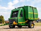 Green round baler with yellow stripes parked in a dry hay field, ready for baler hauling and farm equipment transport