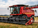 Red combine harvester with a wide draper header parked on green grass, ready for farm equipment hauling and combine transport