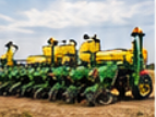 Green multi-row crop planter with yellow seed hoppers parked on a dirt field, ready for farm equipment hauling and planter transport