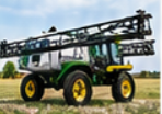 Green self-propelled crop sprayer with folded booms and a white tank on grass, ready for sprayer hauling and farm equipment transport