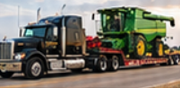 Black semi truck hauling a green combine harvester on a red step deck trailer for combine harvester transport