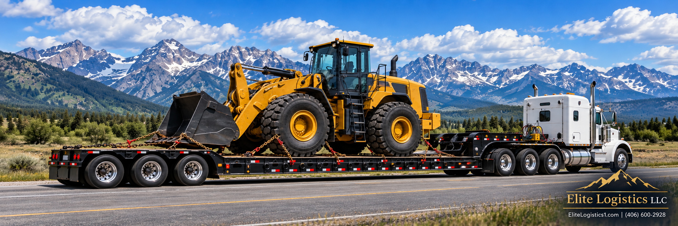 Yellow wheel loader secured on a lowboy trailer pulled by a white semi-truck against a mountain backdrop.